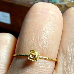 May include: A delicate gold ring with a small rose-shaped design. The ring is worn on a finger.