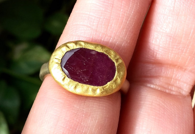 May include: A gold ring featuring a large, oval ruby gemstone set in a textured gold bezel.