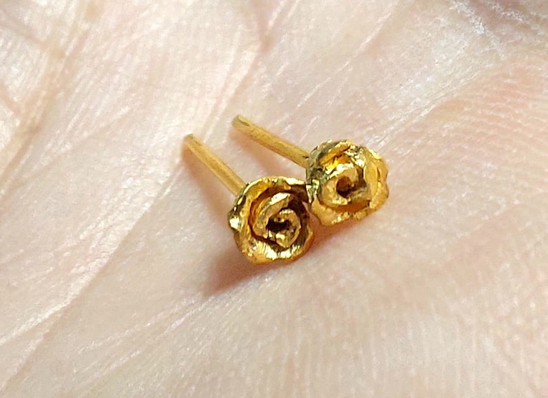 May include: A pair of gold rose stud earrings. The roses are detailed and have a textured finish.