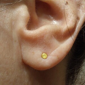 Puede incluir: Primer plano de una oreja con un peque&ntilde;o pendiente redondo de oro.