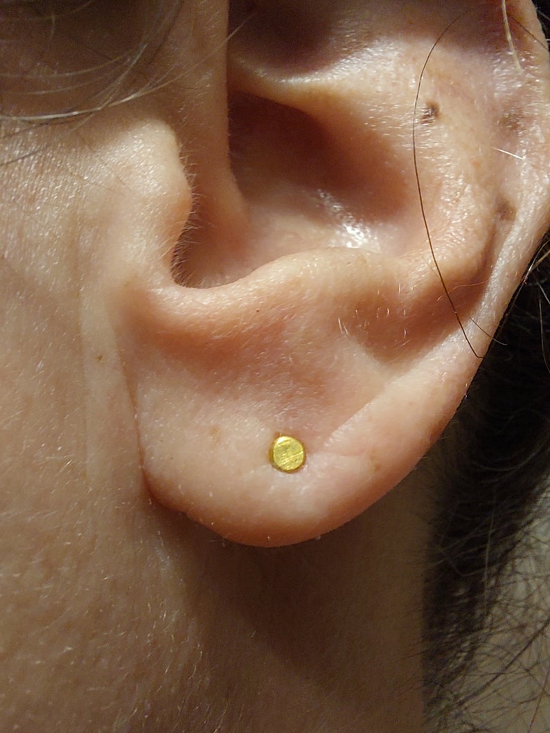 Puede incluir: Primer plano de una oreja con un peque&ntilde;o pendiente redondo de oro.