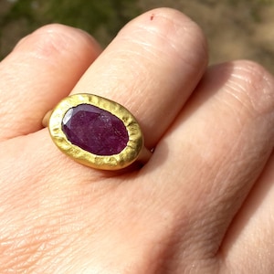 May include: A gold ring featuring a large, oval-shaped, deep purple gemstone set in a textured gold setting.