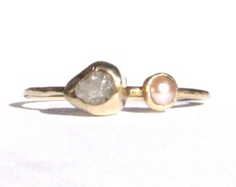May include: A gold ring featuring a rough, white diamond and a pink pearl. The ring is simple and elegant.