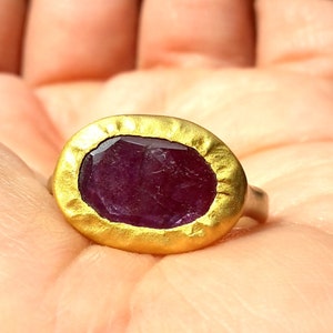 May include: A gold ring featuring a large, oval-shaped, purple gemstone set in the centre.