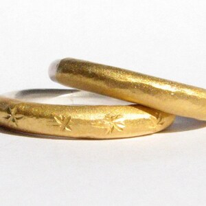 May include: Two gold wedding bands, one with a hammered finish and the other with a star pattern.