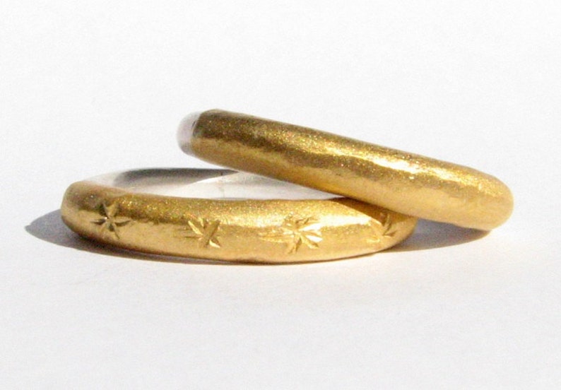 May include: Two gold wedding bands, one with a hammered finish and the other with a star pattern.