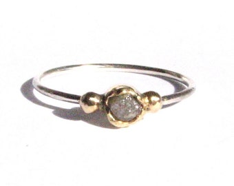 May include: A silver ring with a rough, gray diamond set in a gold bezel. The ring has two gold beads on either side of the diamond.