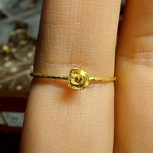 May include: A delicate gold ring with a small rose design. The ring is worn on a finger.