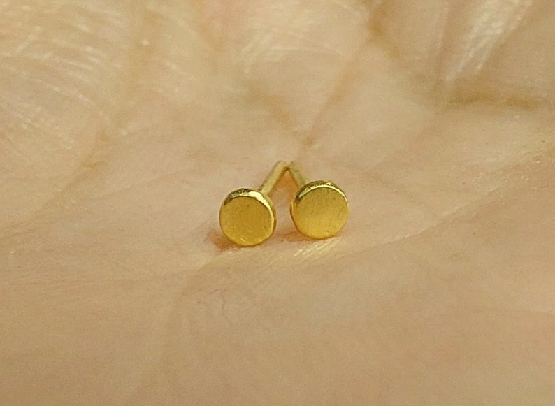 Puede incluir: Un par de peque&ntilde;os pendientes redondos de color dorado. Los pendientes son simples y de dise&ntilde;o minimalista.