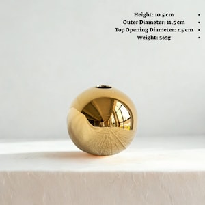 May include: A gold-colored spherical vase with a small opening at the top. The vase is 10.5 cm high, with an outer diameter of 11.5 cm, and a top opening diameter of 2.5 cm. It weighs 565g. The surface reflects the surrounding environment. Home decor.