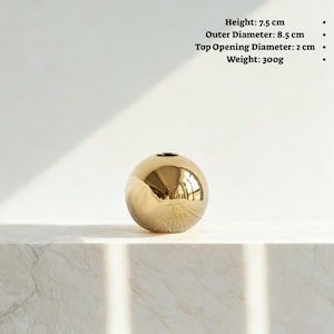 May include: A spherical, gold-colored vase with a small opening at the top. The vase is 3 inches tall, with an outer diameter of 3.3 inches. The top opening is 0.8 inches in diameter. The vase weighs 10.6 ounces.