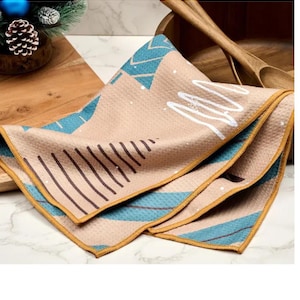 May include: Folded beige kitchen towel with a geometric design featuring blue and brown shapes, and white accents. The towel has a yellow border and is made of a textured material. The towel is likely for kitchen use.