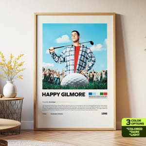 May include: A framed movie poster for "Happy Gilmore" featuring Adam Sandler holding a golf club. The poster has a light wood frame and includes the movie title, a golf ball, and a crowd of people in the background.