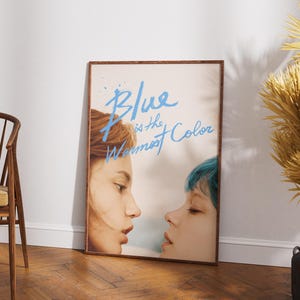 May include: A framed poster with a blue and white title that reads "Blue is the Warmest Color". The poster features a close-up of two women's faces, one with red hair and the other with blue hair.