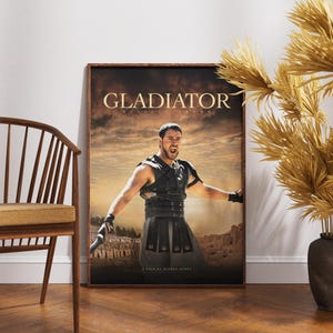 May include: Framed poster for the film "Gladiator" featuring a dramatic image of the main character. The poster has a brown frame and is displayed against a white wall. A wooden chair and decorative plants are in the foreground.
