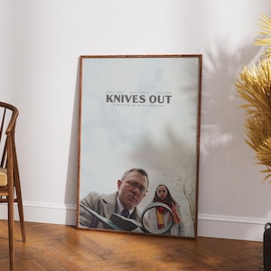 May include: A movie poster for the film "Knives Out" featuring Daniel Craig and Ana de Armas. The poster is framed in a brown wood frame.