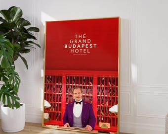 May include: A red poster with gold trim featuring the title "The Grand Budapest Hotel" and a man in a purple suit standing behind a red counter with a key rack.