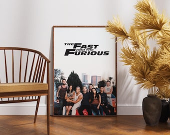 May include: A framed poster for "The Fast and the Furious" movie, featuring a group of actors in front of a city backdrop. The title is prominently displayed in black and white. The poster is leaning against a white wall.