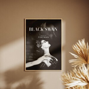 May include: A framed poster featuring the movie title "Black Swan" and the name "Natalie Portman." The black and white image shows a woman in a ballet pose. The poster is displayed on a neutral-toned wall.