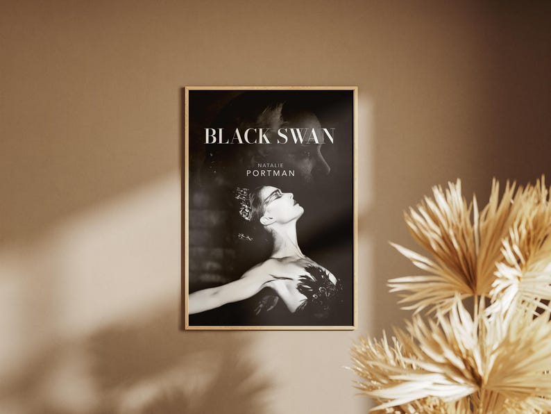 May include: A framed poster featuring the movie title "Black Swan" and the name "Natalie Portman." The black and white image shows a woman in a ballet pose. The poster is displayed on a neutral-toned wall.