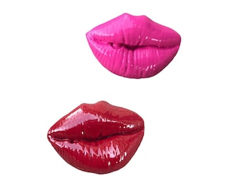 May include: Two pairs of glossy lips, one pink and one red, are shown against a white background. The lips are sculpted and appear to be made of resin.