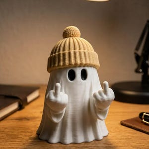 Könnte beinhalten: Eine weiße Geisterfigur mit einer beigen, gerippten Mütze mit Bommel. Der Geist hat zwei schwarze, ovale Augen und hält beide Hände hoch, wobei die Mittelfinger ausgestreckt sind. Die Figur besteht aus einem glatten, matten Material.