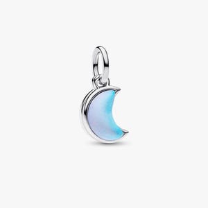 Puede incluir: Un charm de luna creciente plateado con un relleno de esmalte iridiscente azul claro y blanco. El charm tiene un pequeño lazo en la parte superior para sujetarlo a una pulsera o collar. La forma de la luna es lisa y pulida.