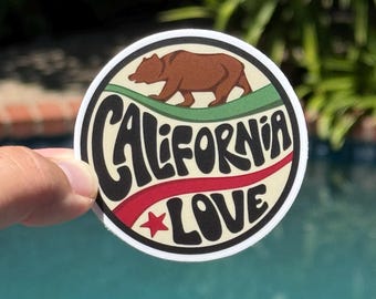 May include: Round sticker with a brown bear on a green background, above the word "CALIFORNIA" in black, and "LOVE" in black with a red star. The sticker has a white border.