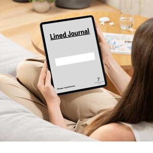 May include: A person is sitting on a couch and holding a tablet. The tablet screen displays the text "Lined Journal" and has a white box for writing. The tablet is black with a white border.