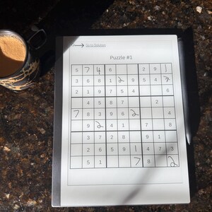 May include: A white sheet of paper with a Sudoku puzzle printed on it. The puzzle is labeled "Puzzle #1" and has numbers 1 through 9 filled in some of the squares. The puzzle is partially solved with some numbers filled in.