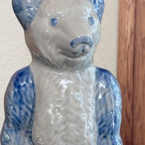 May include: A ceramic bear figurine featuring a glossy finish with a light gray body and vibrant blue accents on the ears, nose, and arms. The bear has a textured surface that mimics fur, with distinct blue eyes and a molded snout and mouth.