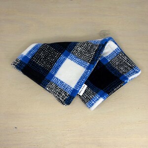 May include: A folded, blue, black, and white plaid fleece neck warmer. The pattern features large squares of white, black, and blue. A small white tag with the text "Bailey & Ben" is visible.