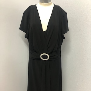 Könnte beinhalten: Ein schwarzes Maxikleid mit V-Ausschnitt und kurzen Ärmeln. Das Kleid hat einen Gürtel mit einem strassbesetzten Schnallenverschluss in der Taille.