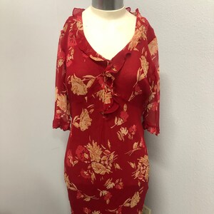 May include: A red floral print dress with a ruffled neckline and sleeves. The dress features a V-neck and a fitted silhouette, with a ruffled hemline. The floral pattern includes beige and pink flowers.