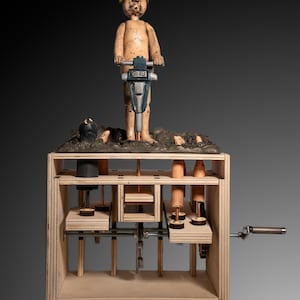 Könnte beinhalten: Holzkinetische Skulptur mit einer Figur, die einen Presslufthammer bedient. Die Figur trägt einen gelben Helm. Die Skulptur hat eine Holzkiste mit beweglichen Teilen und einer Handkurbel. Der Hintergrund ist ein dunkelgrauer Farbverlauf.