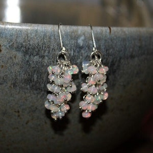 Peut inclure: Une paire de boucles d'oreilles pendantes en argent avec un groupe de pierres d'opale blanches iris&eacute;es.