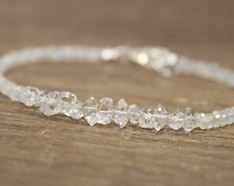 Puede incluir: Un brazalete delicado hecho con cuentas de cristal transparentes y facetadas. Las cuentas están enhebradas en una cadena de plata y están dispuestas en una fila.