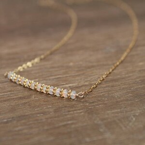 May include: A delicate gold chain necklace with a row of small white opal beads.
