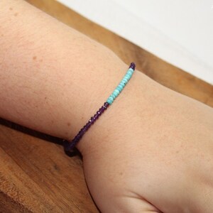 May include: A bracelet with purple and turquoise beads on a person's wrist.