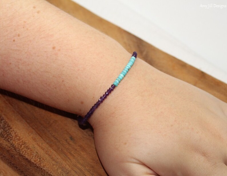 May include: A bracelet with purple and turquoise beads on a person's wrist.