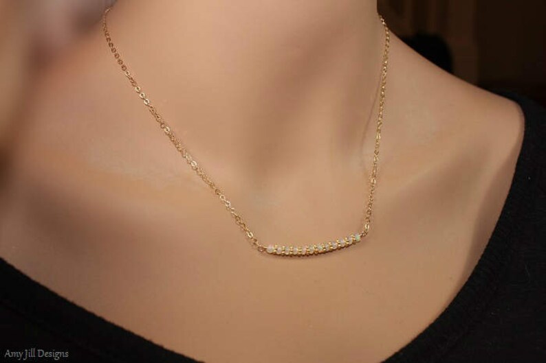 May include: A gold chain necklace with a delicate row of small, clear stones forming a curved bar pendant.
