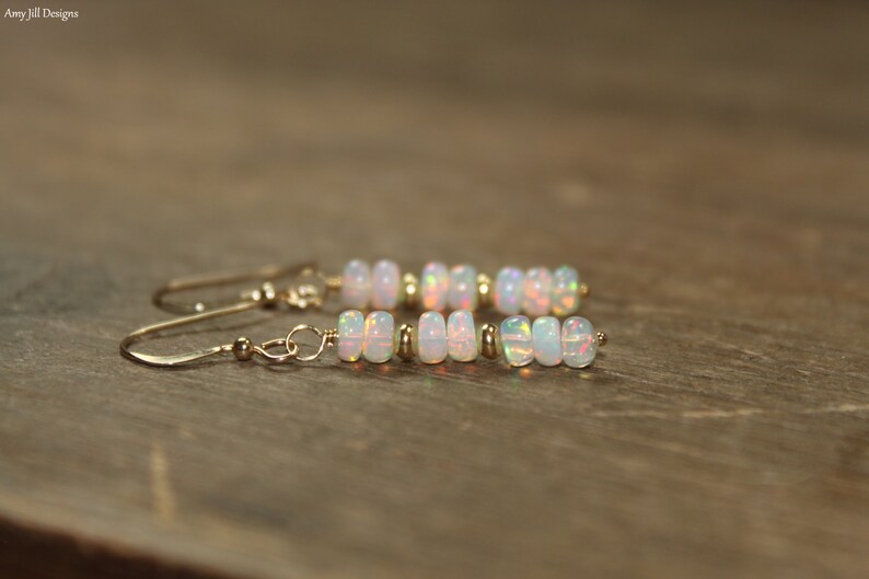 May include: A pair of gold earrings with a row of white opal beads. The earrings have a simple, elegant design.