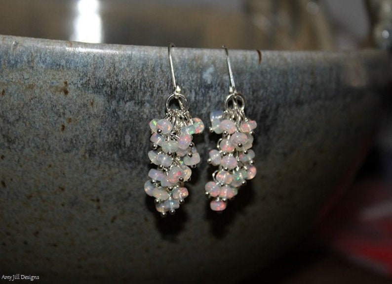 Peut inclure: Une paire de boucles d'oreilles pendantes en argent avec un groupe de pierres d'opale blanches iris&eacute;es.