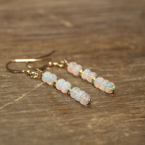 May include: A pair of gold earrings with white opal beads. The earrings are dangle style and have a simple design.