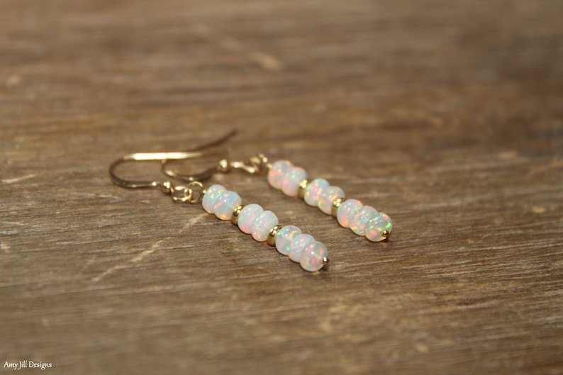 May include: A pair of gold earrings with white opal beads. The earrings are dangle style and have a simple design.