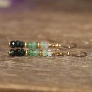 May include: A pair of dangle earrings featuring a gradient of green gemstone beads and gold spacers. The earrings have gold hooks.