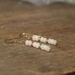 May include: A pair of gold earrings with white opal beads. The earrings are dangle style and have a simple design.