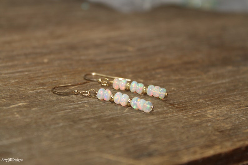 May include: A pair of gold earrings with white opal beads. The earrings are dangle style and have a simple design.