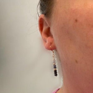 May include: A pair of dangle earrings with a gold hook and a chain with blue and black beads.