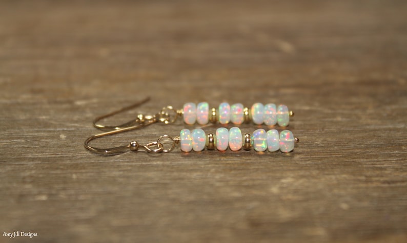 May include: A pair of gold earrings with white opal beads. The earrings are dangle style with a small gold bead at the top.
